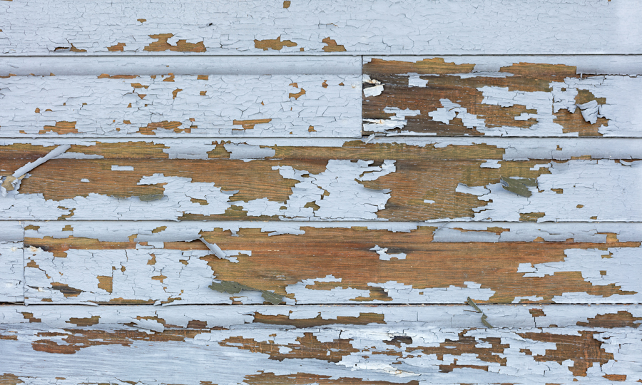 Peeling white paint reveals the weathered texture of an old wooden wall, showcasing its rustic charm and age.