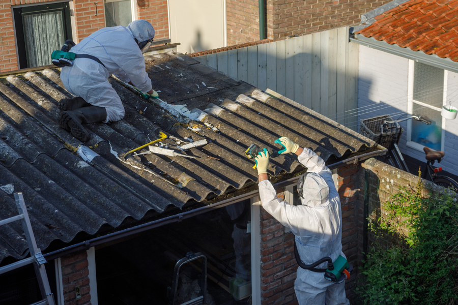 Two men in protective clothing working on a roof, one man is hammering while the other is measuring.