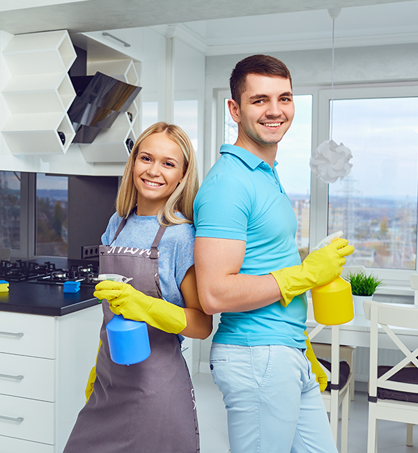 A man and woman stand in a kitchen, each holding cleaning supplies, ready to tackle household chores together.