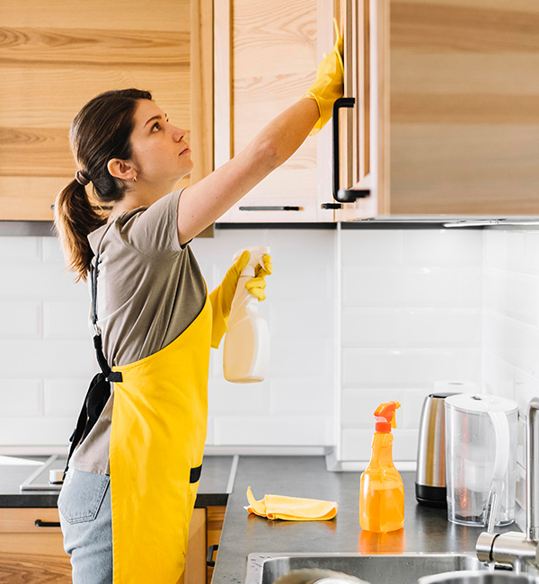 A woman wearing a yellow apron diligently cleans the kitchen, showcasing her commitment to maintaining a tidy space.