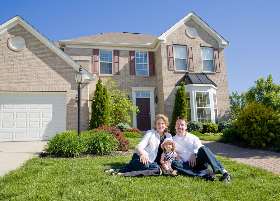 A family joyfully seated in front of their new house, showcasing happiness and togetherness in their new beginning.