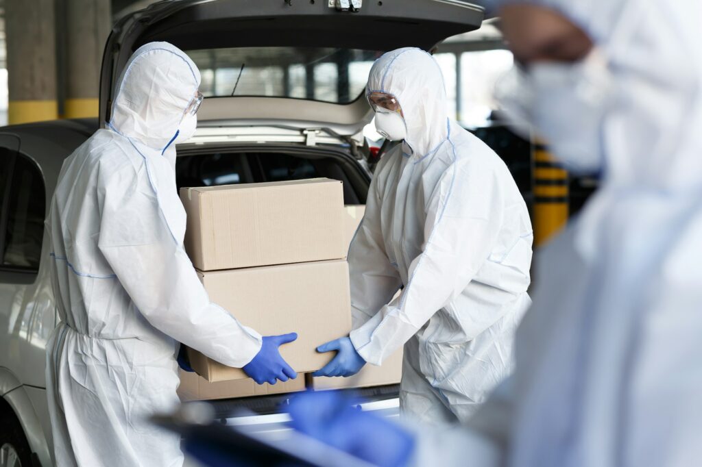 Two individuals in white protective suits and gloves loading boxes into a car.