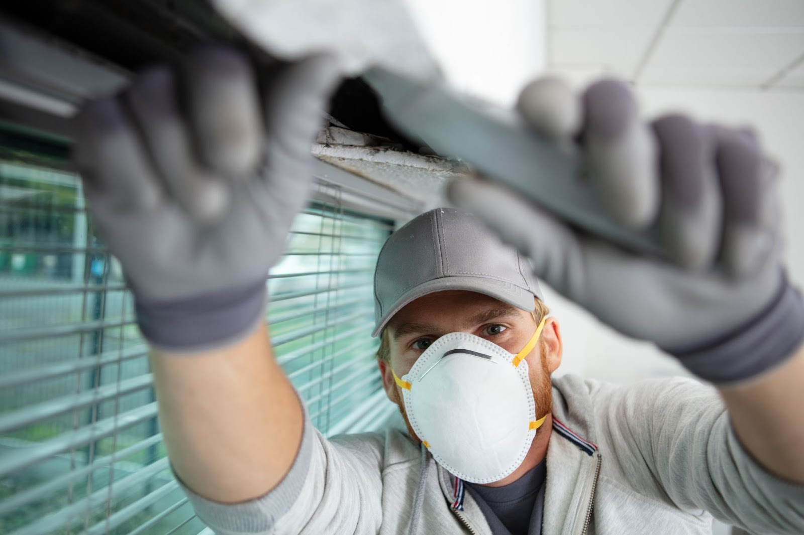 A masked man in gloves repairs a window, ensuring safety during asbestos removal and hazardous material abatement.