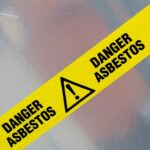 A yellow and black tape marked Danger Asbestos warns of hazardous asbestos exposure and removal risks.