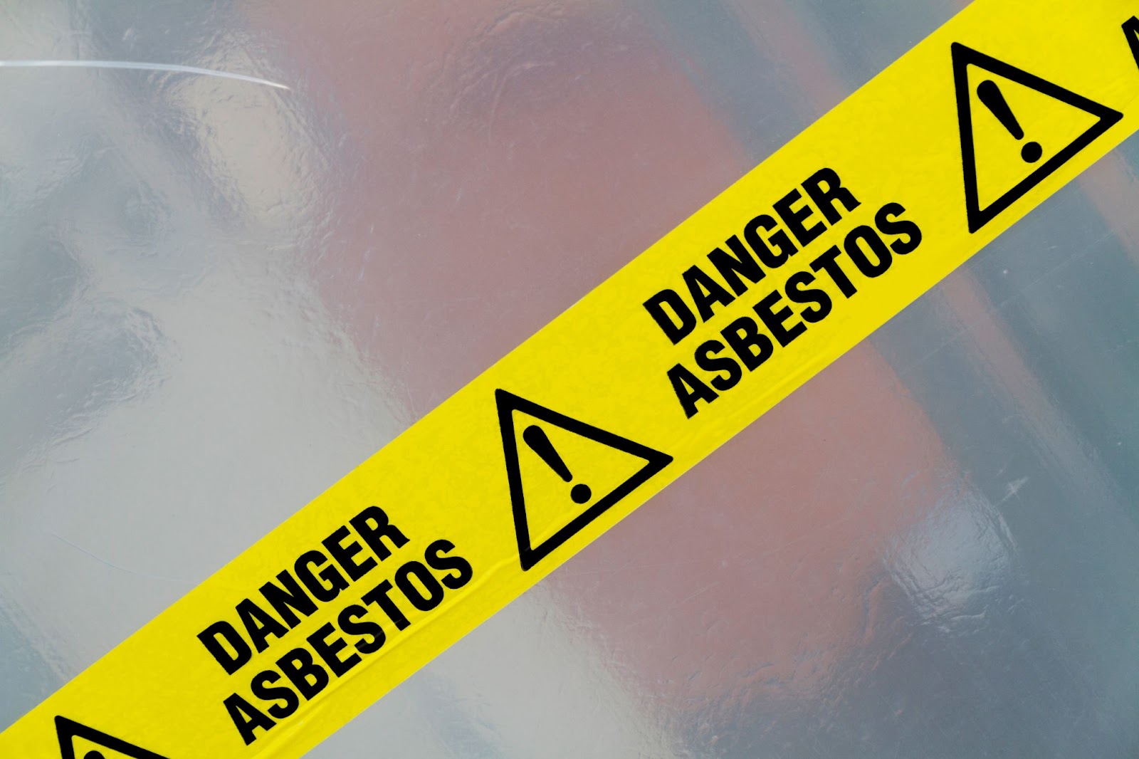 A yellow and black tape marked Danger Asbestos warns of hazardous asbestos exposure and removal risks.