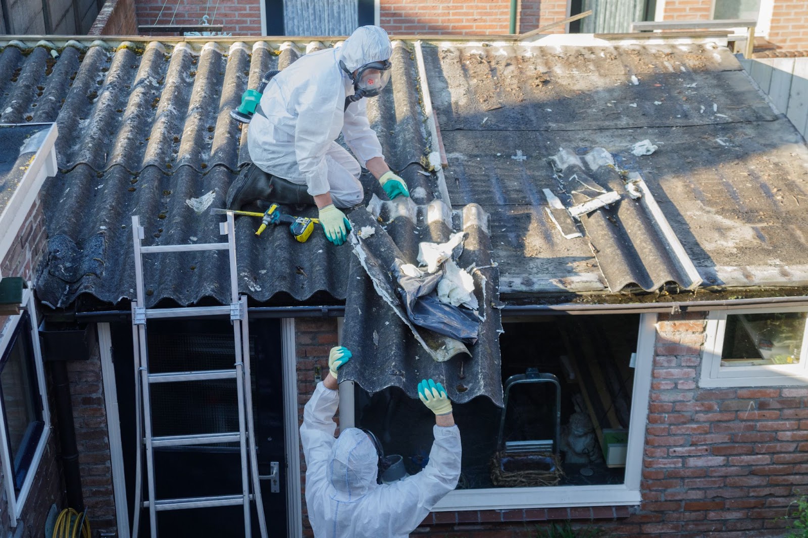 Two men in protective gear safely working on a roof, focused on asbestos removal to prevent exposure risks.